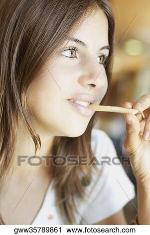 Stock Image - Close-up of a young woman eating French fries and smiling. Fotosearch