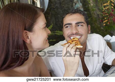 Stock Image - Close-up of a young woman feeding a young man with a pizza slice. Fotosearch