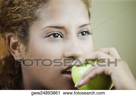 Close-up of a young woman holding an apple in front of her mouth View Large Photo Image Stock Image - Close-up of a young woman holding an apple in front of her mouth. Fotosearch