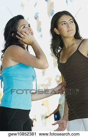 Stock Image - Close-up of a young woman talking on a mobile phone with another woman standing beside her. Fotosearch