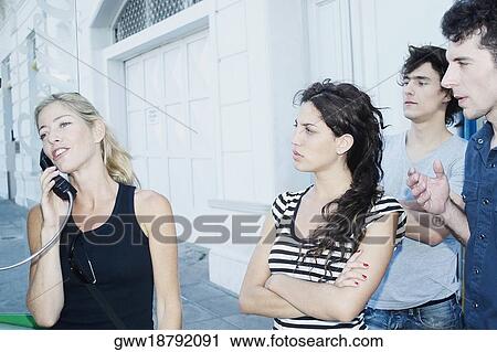 Close-up of a young woman talking on the telephone with her friends standing beside her View Large Photo Image Stock Image - Close-up of a young woman talking on the telephone with her friends standing beside her. Fotosearch