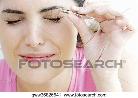 Stock Image - Close-up of a young woman tweezing her eyebrows. Fotosearch