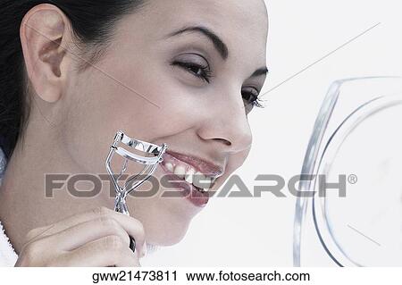 Stock Image - Close-up of a young woman using a eyelash curler and smiling. Fotosearch
