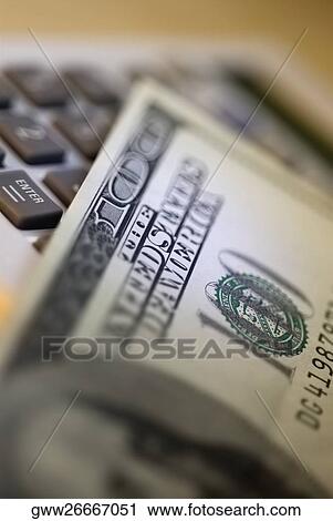 Stock Image - Close-up of one hundred dollar bank note with a calculator. Fotosearch