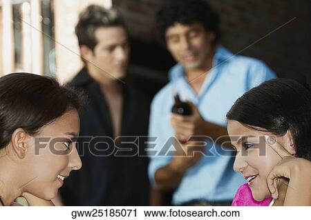Stock Image - Close-up of two teenage girls smiling with two young men standing in the background. Fotosearch