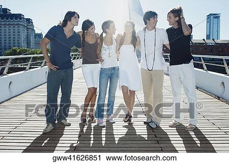 Stock Image - Group of friends with their arms around each other standing on a footbridge. Fotosearch