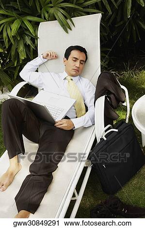 Stock Image - High angle view of a businessman with a laptop sleeping on a lounge chair. Fotosearch