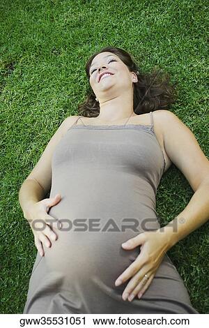 High angle view of a pregnant young woman lying on the grass and touching her abdomen View Large Photo Image Stock Image - High angle view of a pregnant young woman lying on the grass and touching her abdomen. Fotosearch