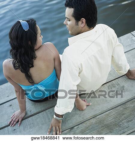 High angle view of a young couple sitting on a pier View Large Photo Image Stock Image - High angle view of a young couple sitting on a pier. Fotosearch