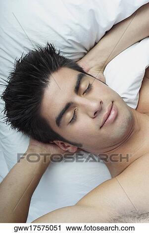 High angle view of a young man sleeping with his hands behind his head View Large Photo Image Stock Image - High angle view of a young man sleeping with his hands behind his head. Fotosearch