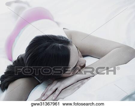Stock Image - High angle view of a young woman lying on the bed. Fotosearch