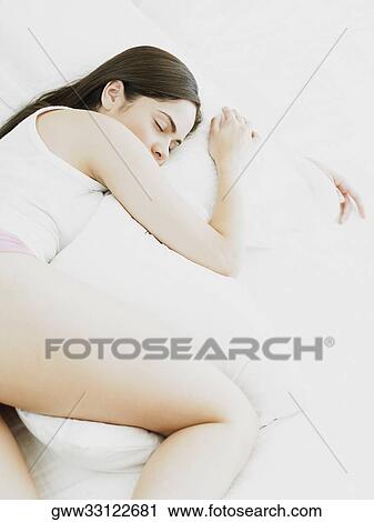Stock Image - High angle view of a young woman lying on the bed and holding a pillow. Fotosearch