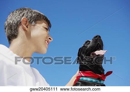 Stock Image - Low angle view of a boy smiling with a dog beside him. Fotosearch