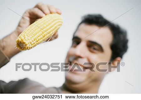 Stock Image - Low angle view of a mid adult man holding a corn. Fotosearch