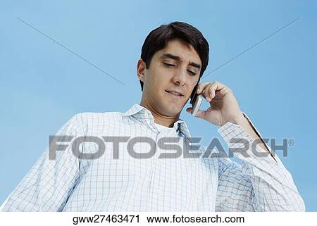 Stock Image - Low angle view of a mid adult man talking on a mobile phone. Fotosearch