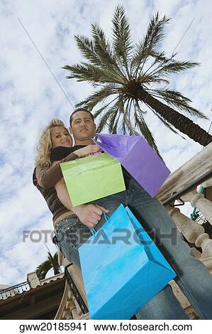 Low angle view of a young couple holding shopping bags and smiling View Large Photo Image Stock Image - Low angle view of a young couple holding shopping bags and smiling. Fotosearch