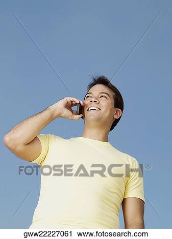 Low angle view of a young man talking on a mobile phone View Large Photo Image Stock Image - Low angle view of a young man talking on a mobile phone. Fotosearch