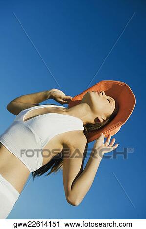 Low angle view of a young woman holding a hat View Large Photo Image Stock Image - Low angle view of a young woman holding a hat. Fotosearch
