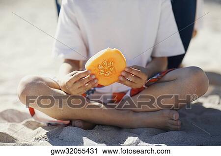 Stock Image - Low section view of a boy holding a slice of melon. Fotosearch
