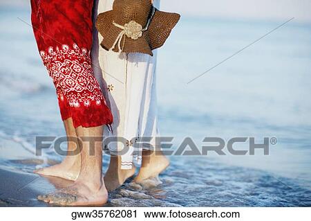 Stock Image - Low section view of a man and a woman standing on the beach. Fotosearch