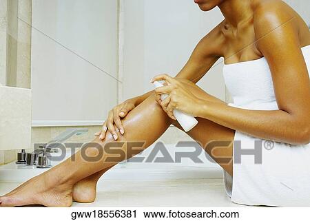 Stock Image - Low section view of a woman applying moisturizer on her leg. Fotosearch