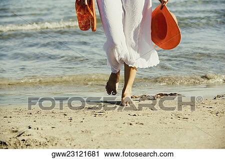 Low section view of a woman holding a hat and a pair of flip-flops on the beach View Large Photo Image Stock Image - Low section view of a woman holding a hat and a pair of flip-flops on the beach. Fotosearch