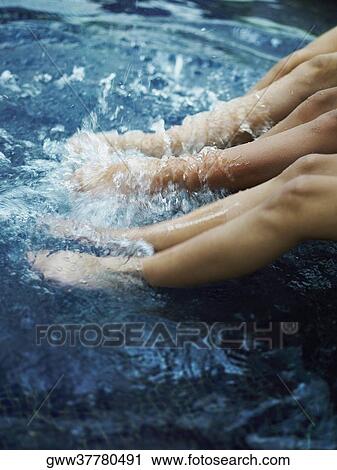 Stock Image - Low section view of three people flapping their legs in water. Fotosearch