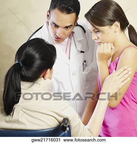 Stock Image - Male doctor talking to a female patient sitting in a wheelchair with her daughter standing beside her. Fotosearch