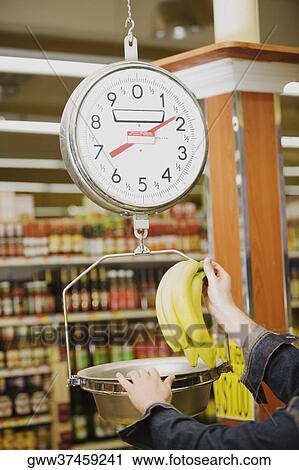 Man's hand weighing a bunch of bananas on a weighing scale in a supermarket View Large Photo Image Stock Image - Man's hand weighing a bunch of bananas on a weighing scale in a supermarket. Fotosearch