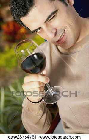 Stock Image - Mid adult man holding a glass of red wine and winking. Fotosearch