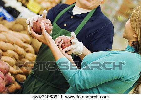Stock Image - Mid section view of a man giving raw potatoes to a young woman. Fotosearch