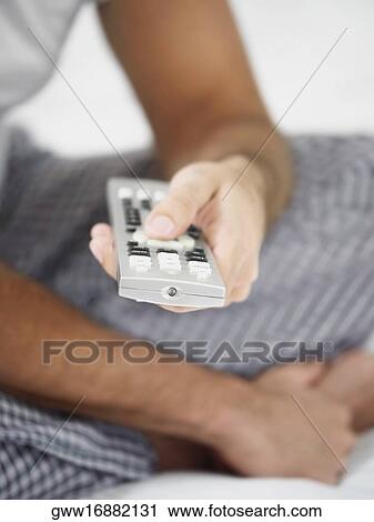 Stock Image - Mid section view of a man holding a remote control. Fotosearch