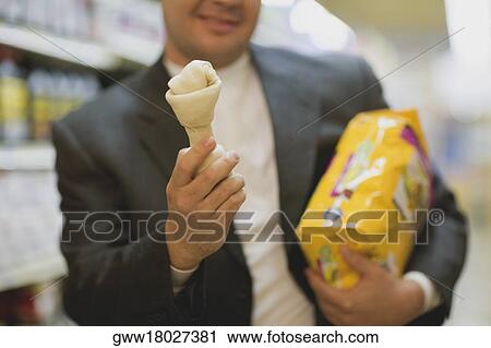 Stock Image - Mid section view of a man holding a packet and a dog bone. Fotosearch