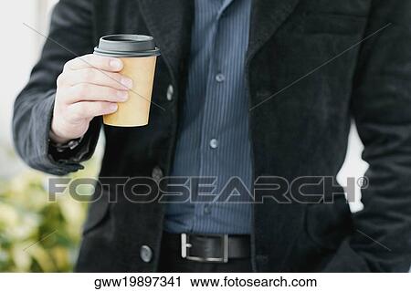 Stock Image - Mid section view of a man holding a disposable cup. Fotosearch