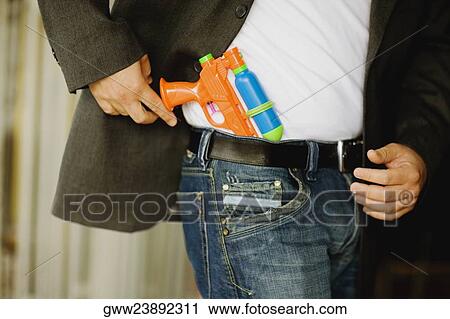 Stock Image - Mid section view of a man holding a squirt gun. Fotosearch
