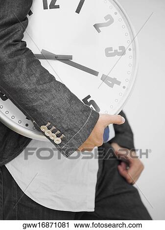 Stock Image - Mid section view of a man holding clock. Fotosearch