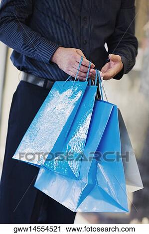 Stock Image - Mid section view of a man holding shopping bags. Fotosearch