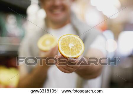 Stock Image - Mid section view of a man holding two pieces of orange. Fotosearch