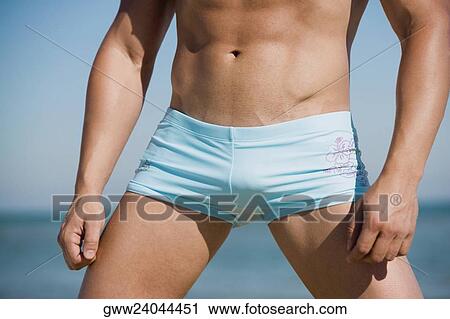 Stock Image - Mid section view of a man standing on the beach. Fotosearch