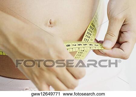 Mid section view of a pregnant woman measuring her abdomen with a tape measure View Large Photo Image Stock Image - Mid section view of a pregnant woman measuring her abdomen with a tape measure. Fotosearch