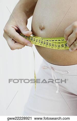 Mid section view of a pregnant woman measuring her abdomen with a tape measure View Large Photo Image Stock Image - Mid section view of a pregnant woman measuring her abdomen with a tape measure. Fotosearch