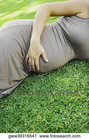 Mid section view of a pregnant woman lying on the grass and touching her abdomen View Large Photo Image Stock Image - Mid section view of a pregnant woman lying on the grass and touching her abdomen. Fotosearch