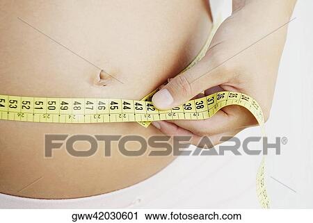Mid section view of a pregnant woman measuring her abdomen with a tape measure View Large Photo Image Stock Image - Mid section view of a pregnant woman measuring her abdomen with a tape measure. Fotosearch