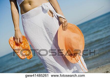 Mid section view of a woman holding hat and a pair of flip-flops on the beach View Large Photo Image Stock Image - Mid section view of a woman holding hat and a pair of flip-flops on the beach. Fotosearch