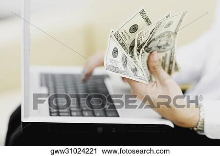 Mid section view of a woman holding paper currency and using a laptop View Large Photo Image Stock Image - Mid section view of a woman holding paper currency and using a laptop. Fotosearch