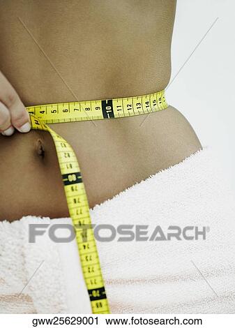 Mid section view of a woman measuring her waist with a tape measure View Large Photo Image Stock Image - Mid section view of a woman measuring her waist with a tape measure. Fotosearch