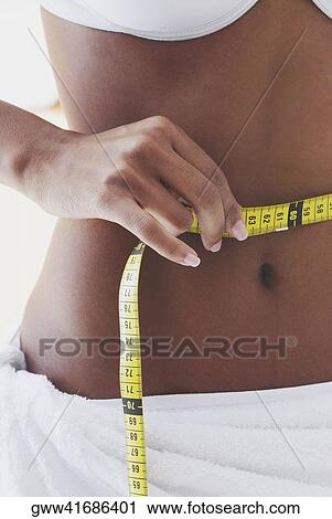 Mid section view of a woman measuring her waist with a tape measure View Large Photo Image Stock Image - Mid section view of a woman measuring her waist with a tape measure. Fotosearch