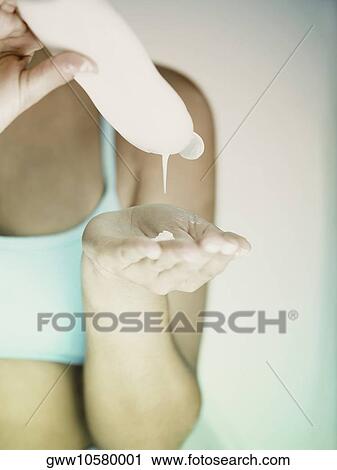 Stock Image - Mid section view of a woman pouring moisturizer in her hand. Fotosearch