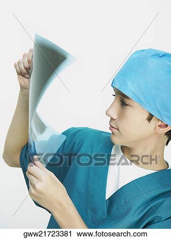 Stock Image - Portrait of a boy wearing surgical scrubs and examining an X-Ray. Fotosearch