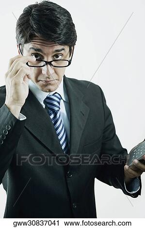Stock Image - Portrait of a businessman peeking over his eyeglasses and holding a calculator. Fotosearch
